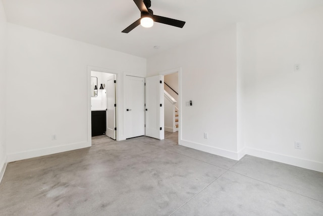 unfurnished bedroom with concrete floors, baseboards, ensuite bath, and a ceiling fan