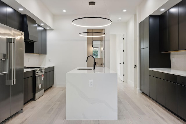 kitchen with appliances with stainless steel finishes, wall chimney range hood, a sink, modern cabinets, and dark cabinets