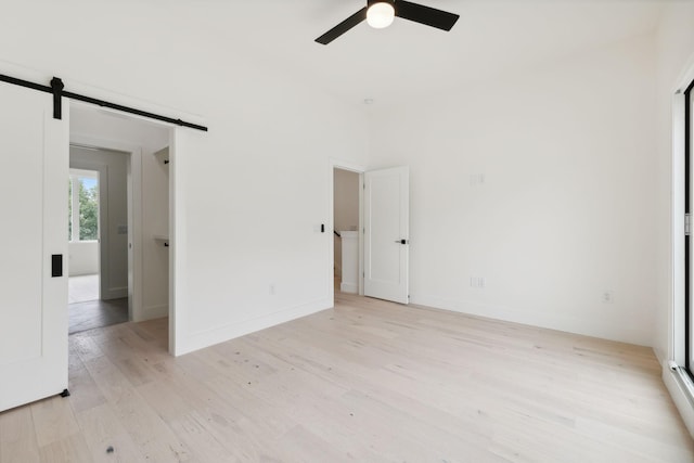 empty room featuring a barn door, a ceiling fan, light wood-style floors, and baseboards