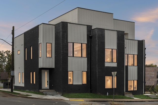 modern home featuring brick siding, entry steps, board and batten siding, and central AC