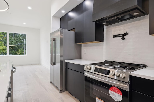 kitchen with stainless steel appliances, wall chimney exhaust hood, light countertops, dark cabinetry, and recessed lighting