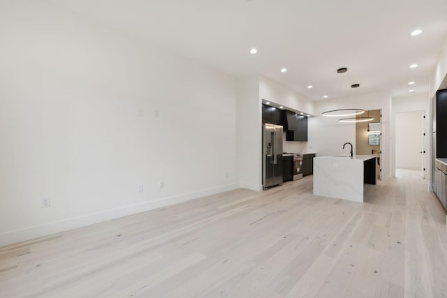 kitchen with light wood finished floors, an island with sink, high end fridge, light countertops, and recessed lighting