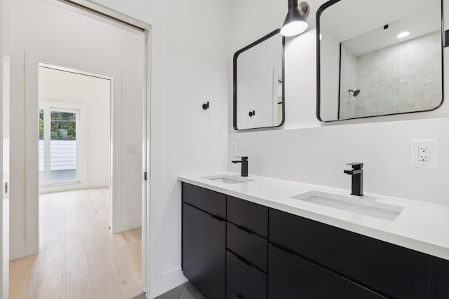 bathroom featuring wood finished floors, double vanity, a shower, and baseboards
