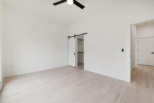 unfurnished bedroom featuring light wood-type flooring, a barn door, ceiling fan, and baseboards