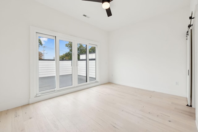 unfurnished room with light wood-type flooring, a barn door, and ceiling fan