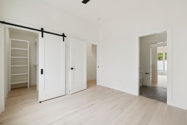 unfurnished bedroom with a barn door, light wood-type flooring, and baseboards