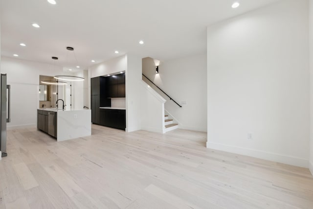 unfurnished living room with light wood-style flooring, stairs, baseboards, recessed lighting, and a sink