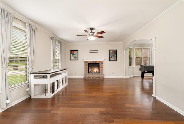unfurnished living room featuring a ceiling fan, plenty of natural light, wood finished floors, a brick fireplace, and ornamental molding