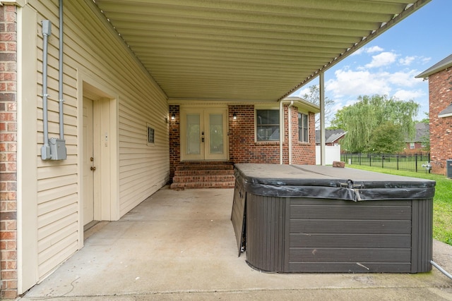 view of patio / terrace with a hot tub, fence, entry steps, and a carport