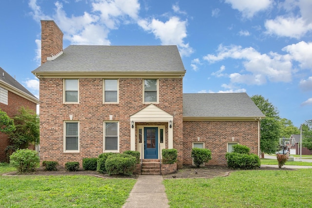 view of front of home featuring a front lawn, brick siding, a chimney, and roof with shingles