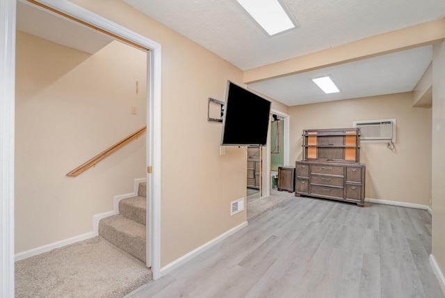 basement with an AC wall unit, baseboards, wood finished floors, and stairway