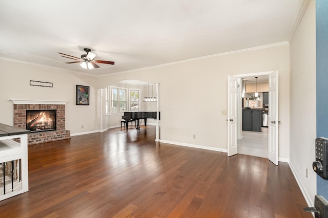 unfurnished living room featuring ceiling fan, crown molding, dark wood-style floors, baseboards, and arched walkways