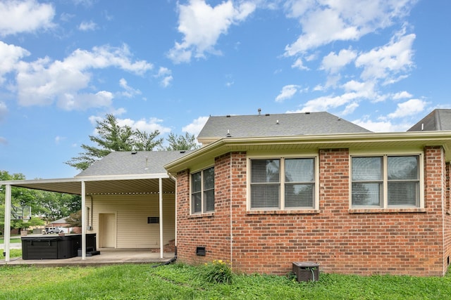 rear view of property featuring a hot tub, a patio area, brick siding, and roof with shingles