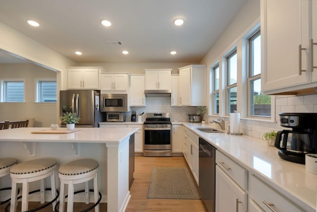kitchen featuring appliances with stainless steel finishes, a sink, a kitchen breakfast bar, white cabinetry, and light wood finished floors
