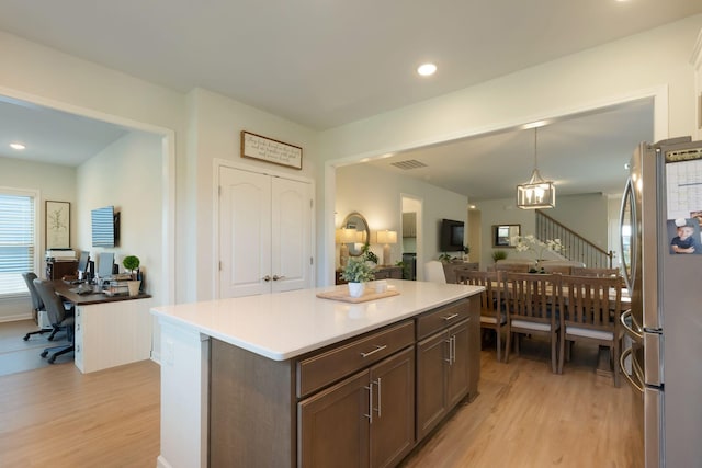 kitchen with freestanding refrigerator, light wood finished floors, an office area, a kitchen island, and decorative light fixtures