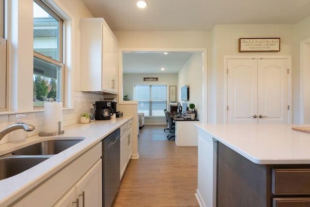 kitchen featuring dishwasher, a sink, light wood-style floors, white cabinetry, and decorative backsplash