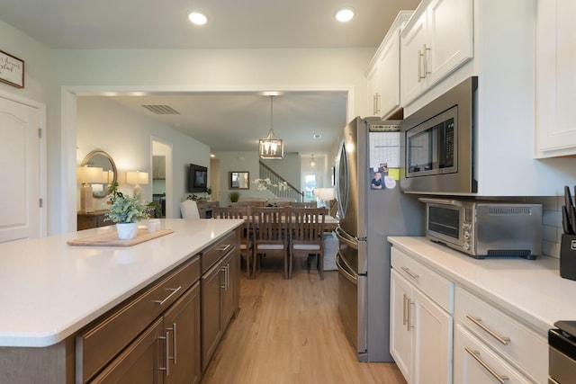 kitchen featuring appliances with stainless steel finishes, white cabinetry, light countertops, light wood-style floors, and decorative light fixtures