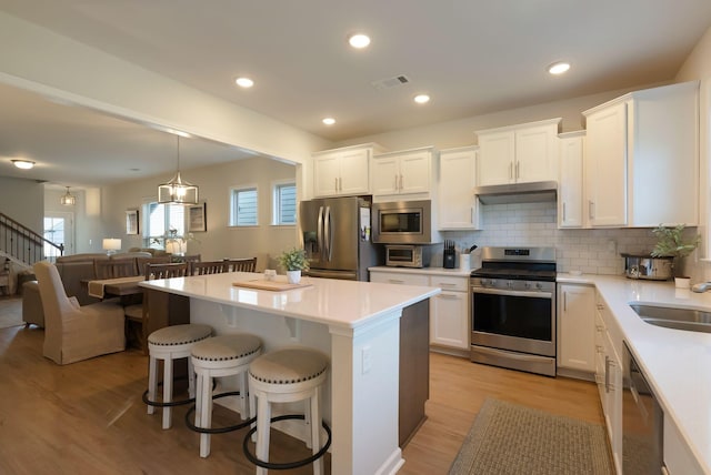 kitchen featuring appliances with stainless steel finishes, under cabinet range hood, white cabinetry, light wood-style flooring, and recessed lighting