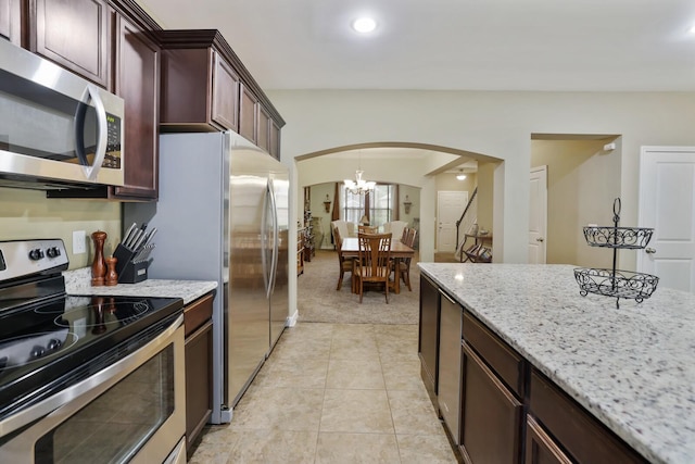 kitchen with stainless steel appliances, arched walkways, light colored carpet, light stone countertops, and recessed lighting