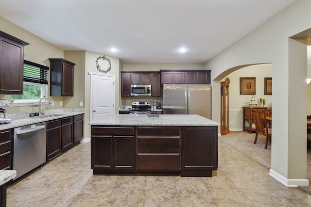 kitchen featuring stainless steel appliances, a sink, arched walkways, a center island, and light stone counters