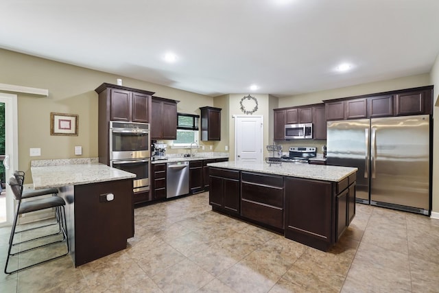 kitchen featuring stainless steel appliances, a peninsula, dark brown cabinetry, light stone countertops, and recessed lighting