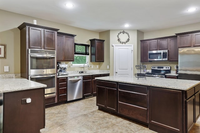 kitchen with stainless steel appliances, a sink, a center island, recessed lighting, and light stone countertops