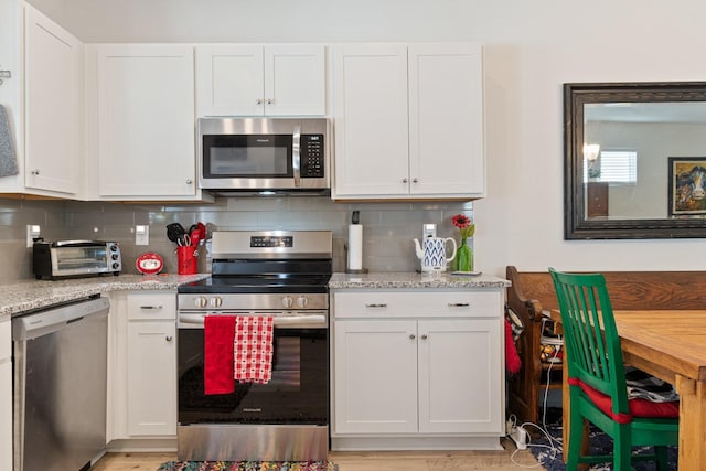kitchen with stainless steel appliances, white cabinetry, decorative backsplash, and light stone counters