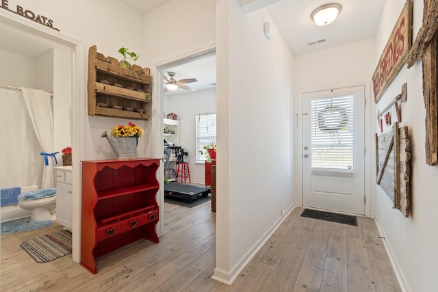 doorway to outside featuring light wood finished floors, a ceiling fan, and baseboards