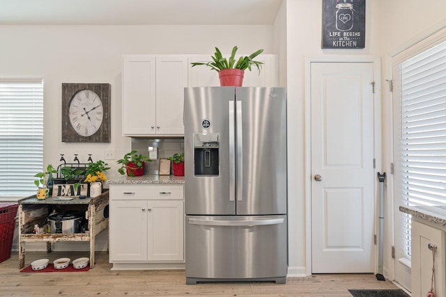 kitchen featuring stainless steel fridge with ice dispenser, light wood finished floors, white cabinets, and light stone countertops