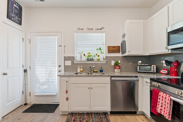 kitchen with stainless steel appliances, a sink, white cabinets, and light wood-style flooring