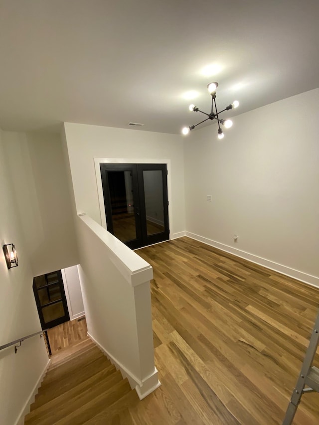 spare room featuring a chandelier, wood finished floors, baseboards, and stairs