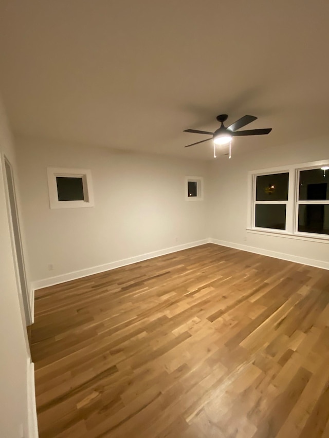 empty room with wood finished floors, a ceiling fan, and baseboards