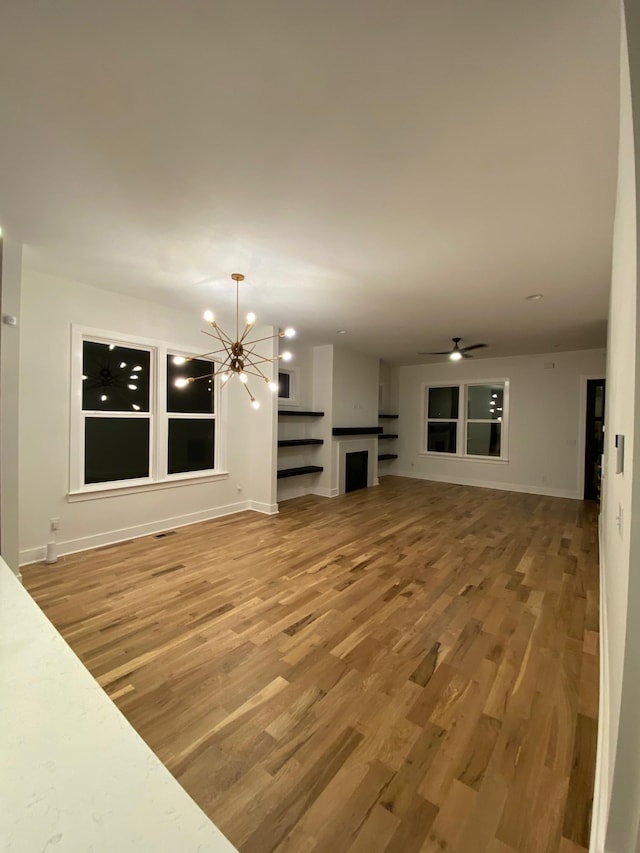 unfurnished living room with light wood finished floors, a chandelier, and baseboards