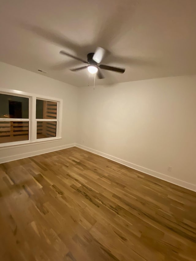 empty room with wood finished floors, a ceiling fan, and baseboards
