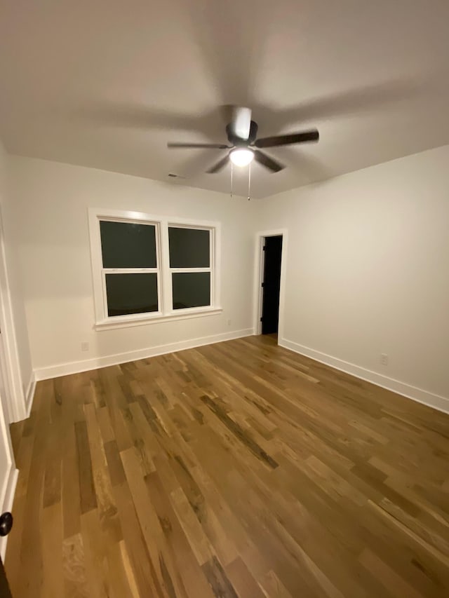 empty room with wood finished floors, a ceiling fan, and baseboards