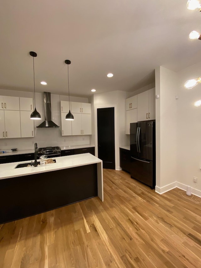 kitchen with wall chimney range hood, freestanding refrigerator, a sink, light countertops, and light wood-type flooring