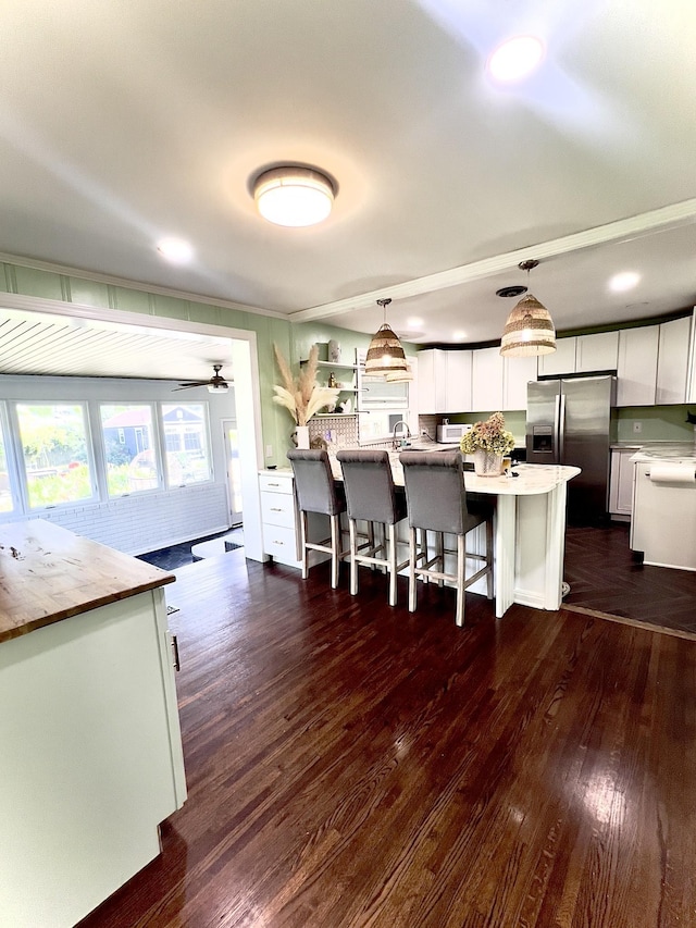 kitchen with stainless steel fridge, white cabinets, a breakfast bar area, dark wood-style flooring, and pendant lighting