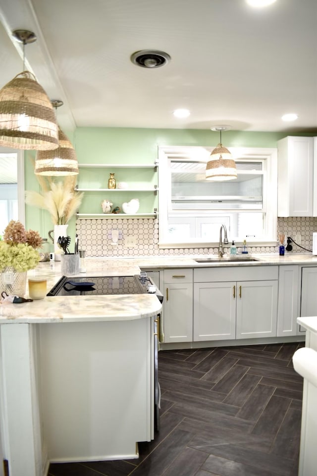 kitchen with a sink, backsplash, white cabinetry, light countertops, and pendant lighting