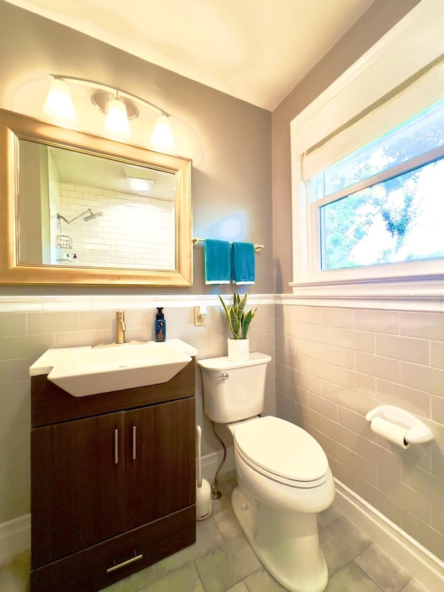 bathroom with tile walls, tile patterned flooring, toilet, vanity, and wainscoting