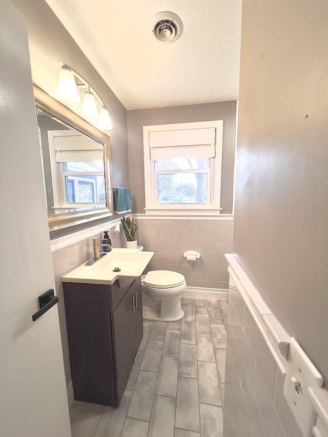 bathroom featuring tile walls, toilet, vanity, and wainscoting