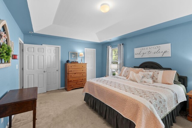 bedroom featuring light carpet, a tray ceiling, and baseboards