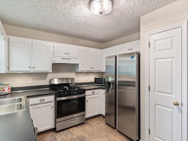 kitchen featuring stainless steel appliances, under cabinet range hood, dark countertops, white cabinetry, and a textured ceiling