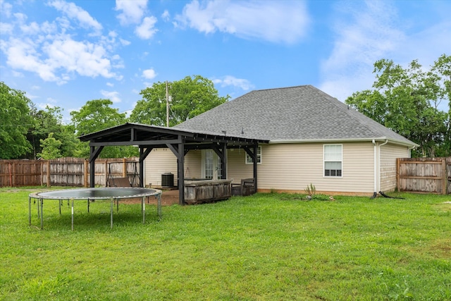 rear view of property featuring central AC, roof with shingles, a gazebo, a trampoline, and a hot tub