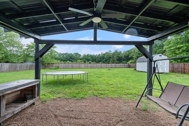view of yard featuring a storage shed, an outdoor structure, a ceiling fan, view of scattered trees, and a trampoline