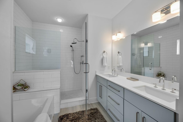 bathroom featuring a stall shower, wood finished floors, double vanity, a tub, and baseboards