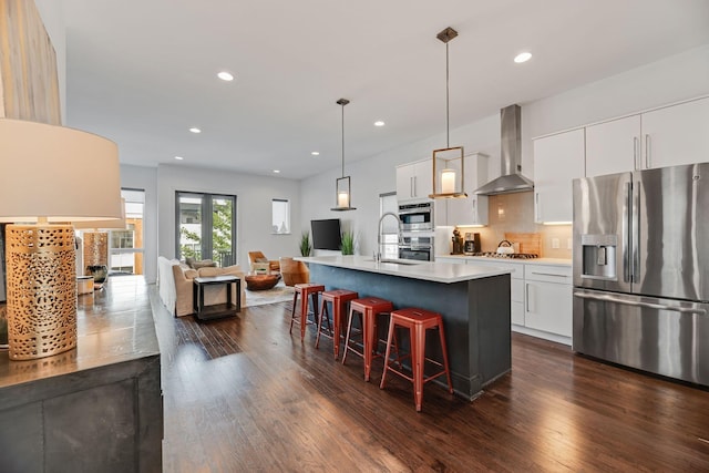 kitchen with appliances with stainless steel finishes, wall chimney exhaust hood, a sink, a kitchen breakfast bar, and dark wood finished floors