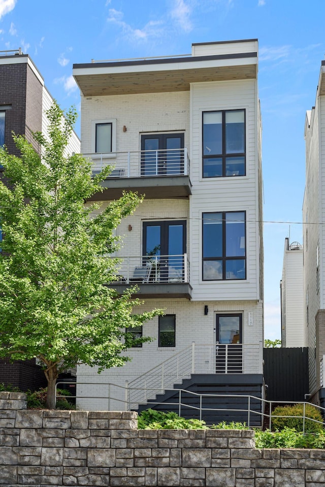 view of front of property with a balcony, brick siding, and fence