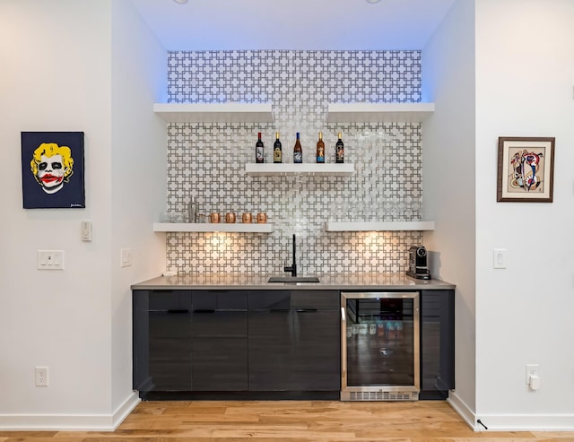 indoor bar featuring beverage cooler, decorative backsplash, light wood finished floors, and baseboards