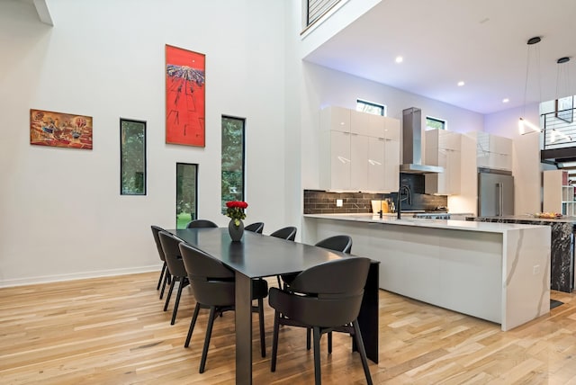 dining room featuring a towering ceiling, light wood-style flooring, baseboards, and recessed lighting