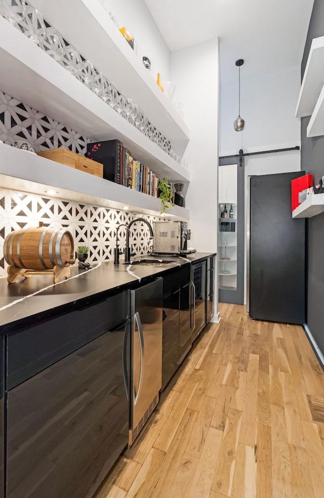 bar area with a barn door, light wood-style floors, refrigerator, a sink, and decorative light fixtures